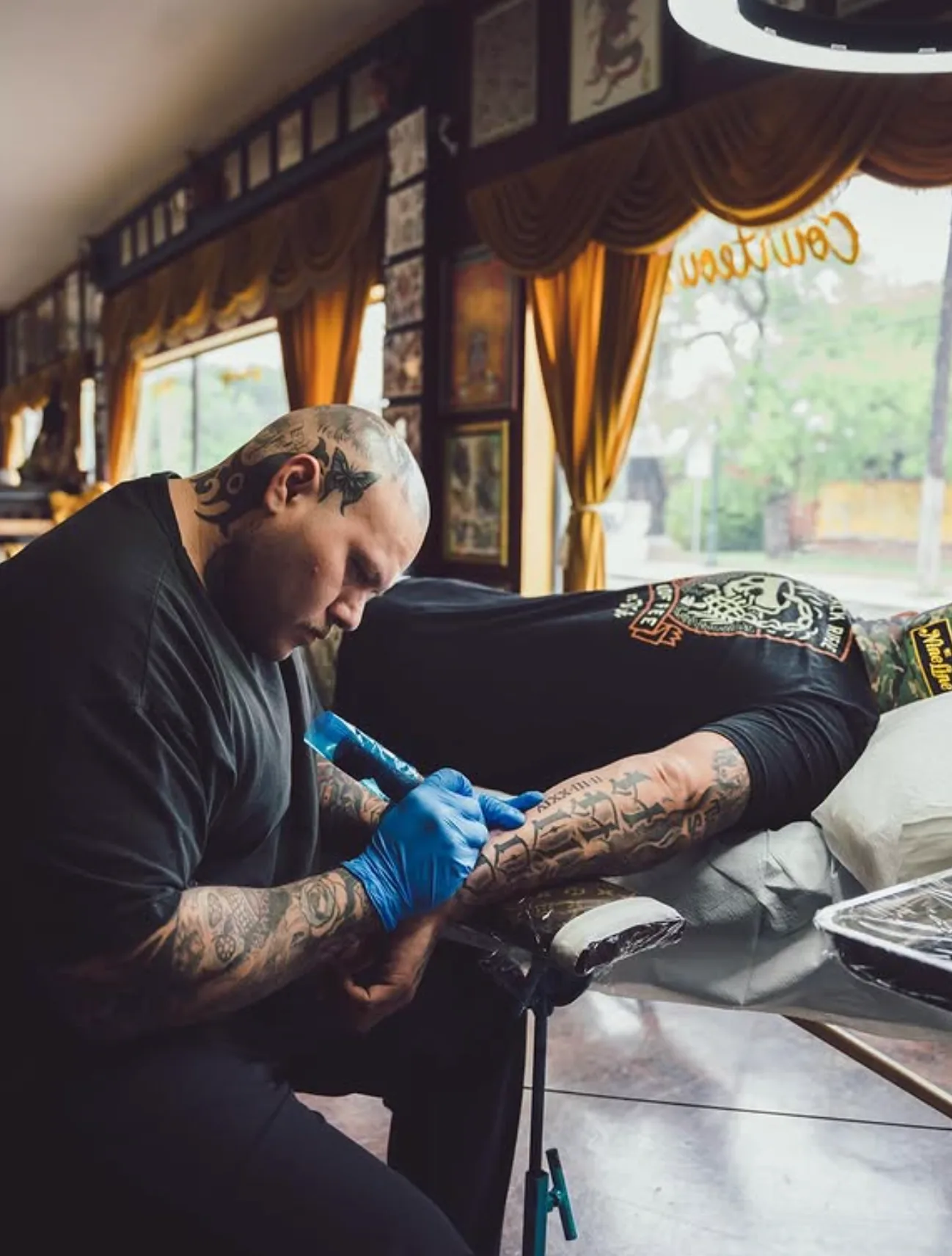 Armando Garza tattooing a client by the front windows at Eternal Courage Tattoo